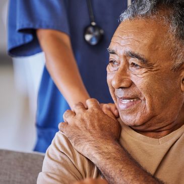 elderly man seated, while holding hands with a woman in a medical uniform and stethoscope 