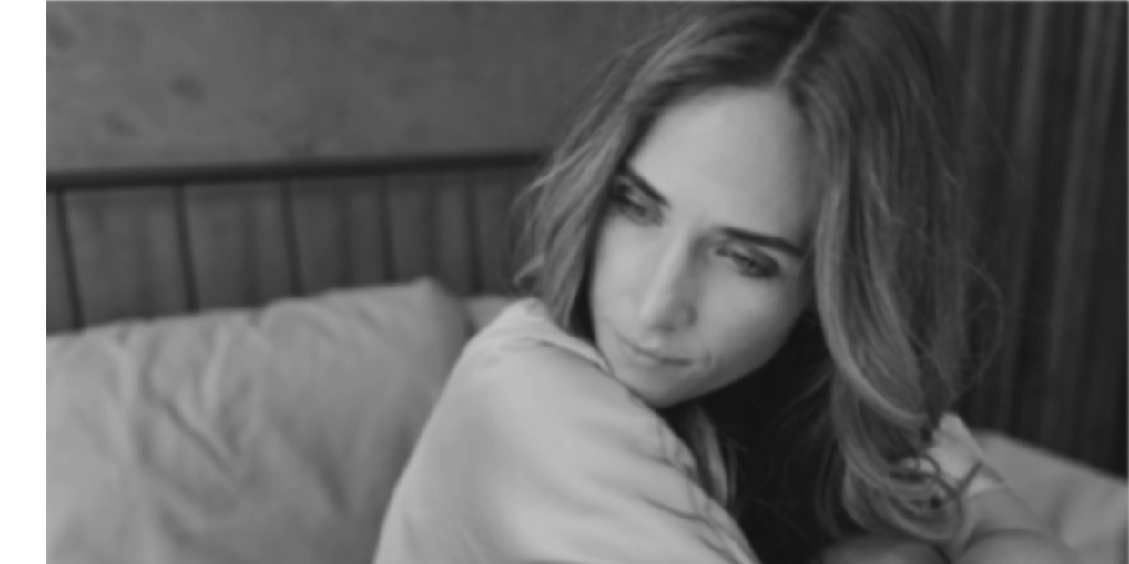 blurred black and white photo of woman somberly gazing to the side while sitting on a bed
