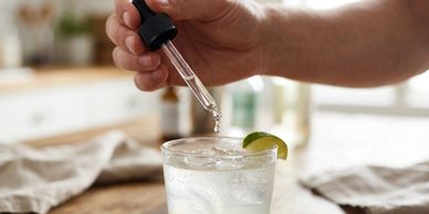 hand with a liquid dropper putting a substance into a drink