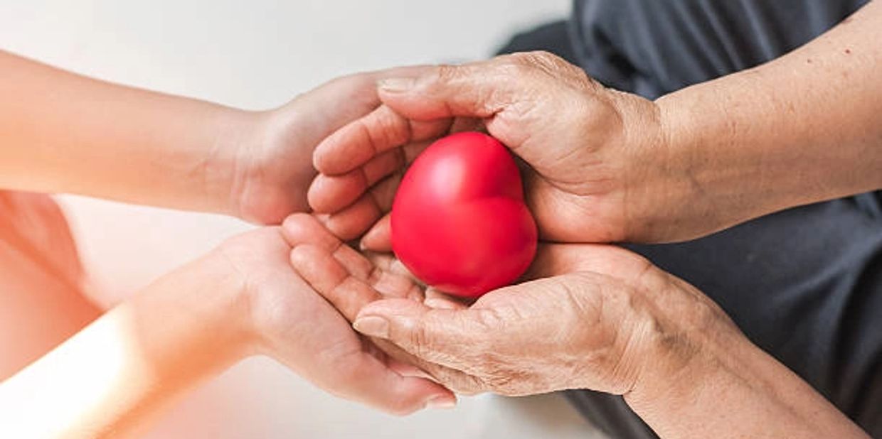 Young and old hands holding a red heart together symbolizing care and love.