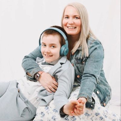 Smiling woman hugging a boy wearing headphones.