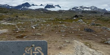 Mountain landscape with a hiking trail sign in foreground.