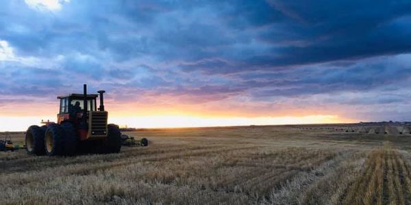 Tractor in a harvested field during sunset under a dramatic sky.