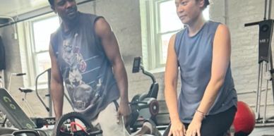 Two people exercising together in a gym with equipment around.