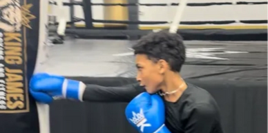 Young boxer practicing a high kick with blue gloves in a gym.