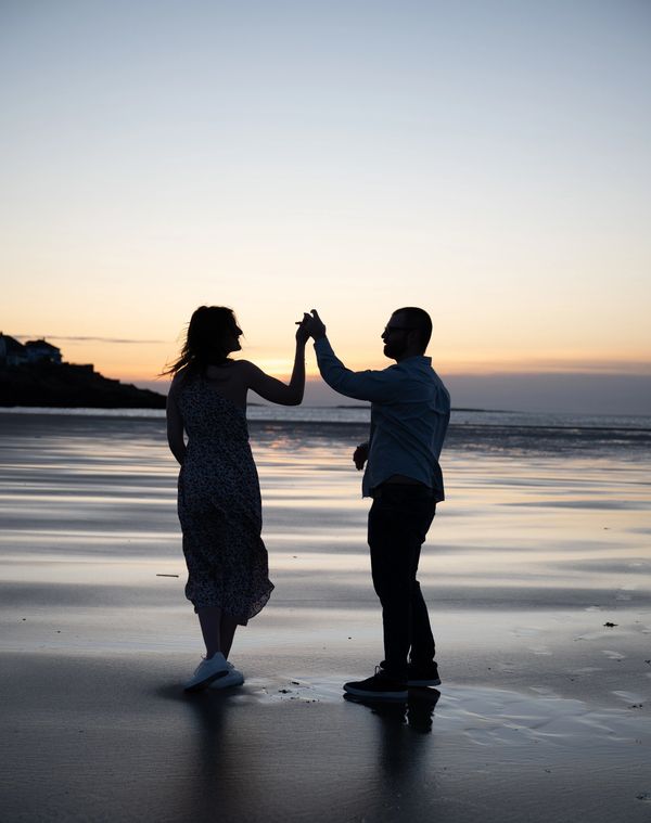 Couple dancing on the beach at sunset, silhouetted against the sky.
