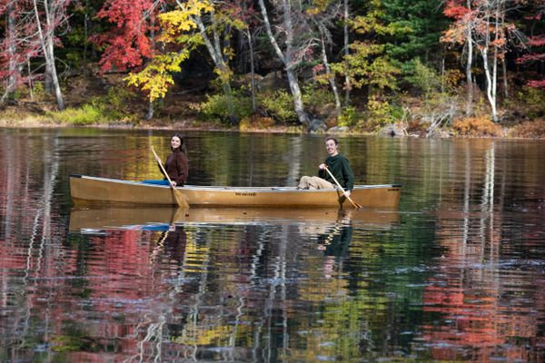 Two people canoeing on a calm lake surrounded by colorful autumn trees.