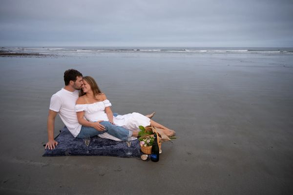 Couple enjoying a romantic beach picnic with champagne and flowers.