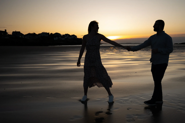 Couple holding hands and walking on the beach at sunset.