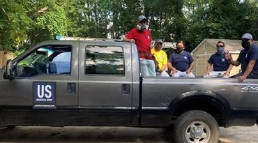 A group of men are sitting in the back of a Ford-250 Truck in US Industrial Group branded shirts.