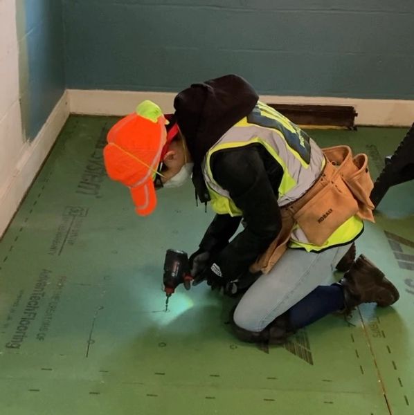 Woman drilling down floor boards with screwdriver.