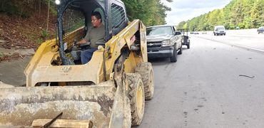 A man is driving a large bulldozer on the road where other cars are traveling. 