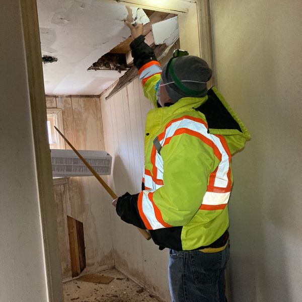 A man removes ceiling tile during exploratory analysis of existing structures.