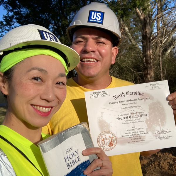 Man and woman smiling, holding NC General Contractor License for Commercial Building and Highway.