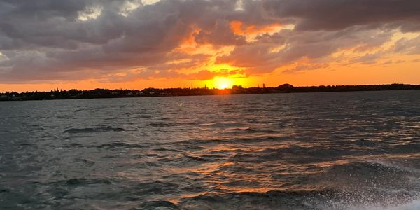 Sunset over a body of water with clouds and distant shoreline.