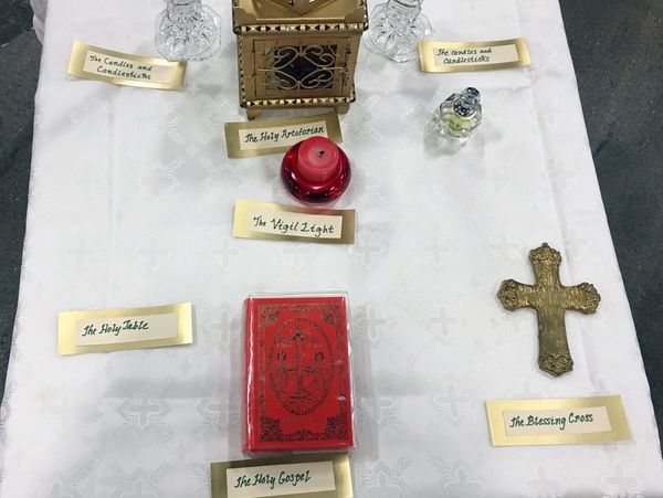 A religious display with labeled items including a cross, holy gospel, vigil light, and candlesticks on a white cloth.