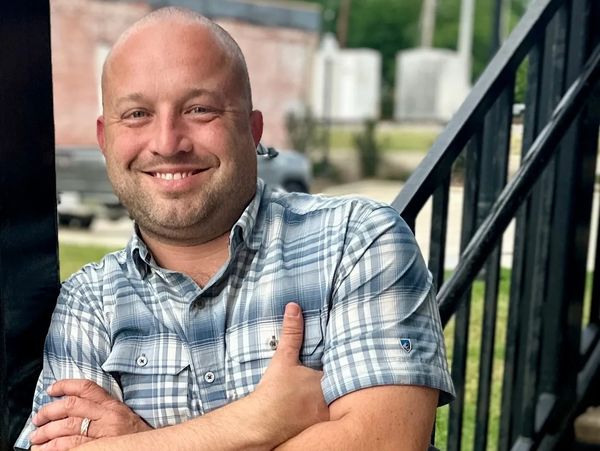 Smiling man in a plaid shirt with folded arms outdoors.