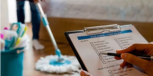 Person checking off a cleaning checklist while another mops the floor.