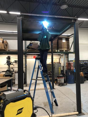 Person welding on a ladder in a workshop.