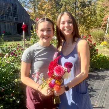 Two young women smiling outdoors with a colorful flower bouquet.