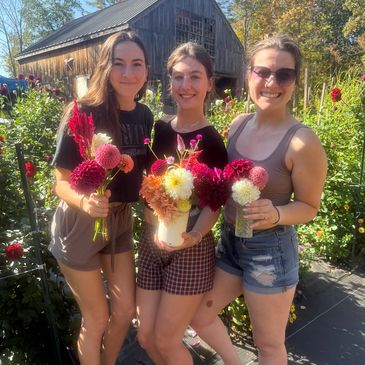 Three young women holding colorful flowers, smiling outdoors in a garden.