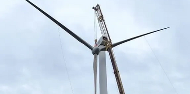 A crane is installing a blade on a wind turbine against a cloudy sky.