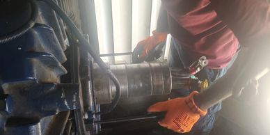 Worker in orange gloves fixing a machine part indoors with tools scattered around.