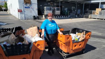 A woman stands outdoors with large carts filled with items.