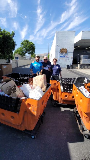 Three people standing behind carts full of bags outdoors.
