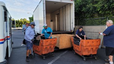 Workers unload mail carts from a truck.