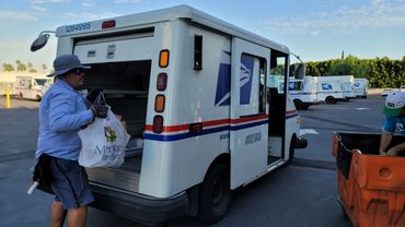USPS worker handling mail delivery vehicle.