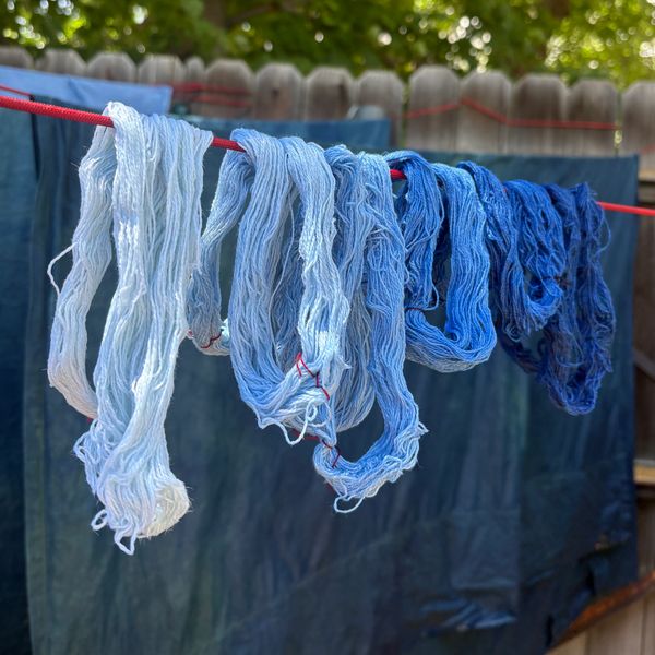 Yarn dyed in gradient shades of blue hanging on a red line.