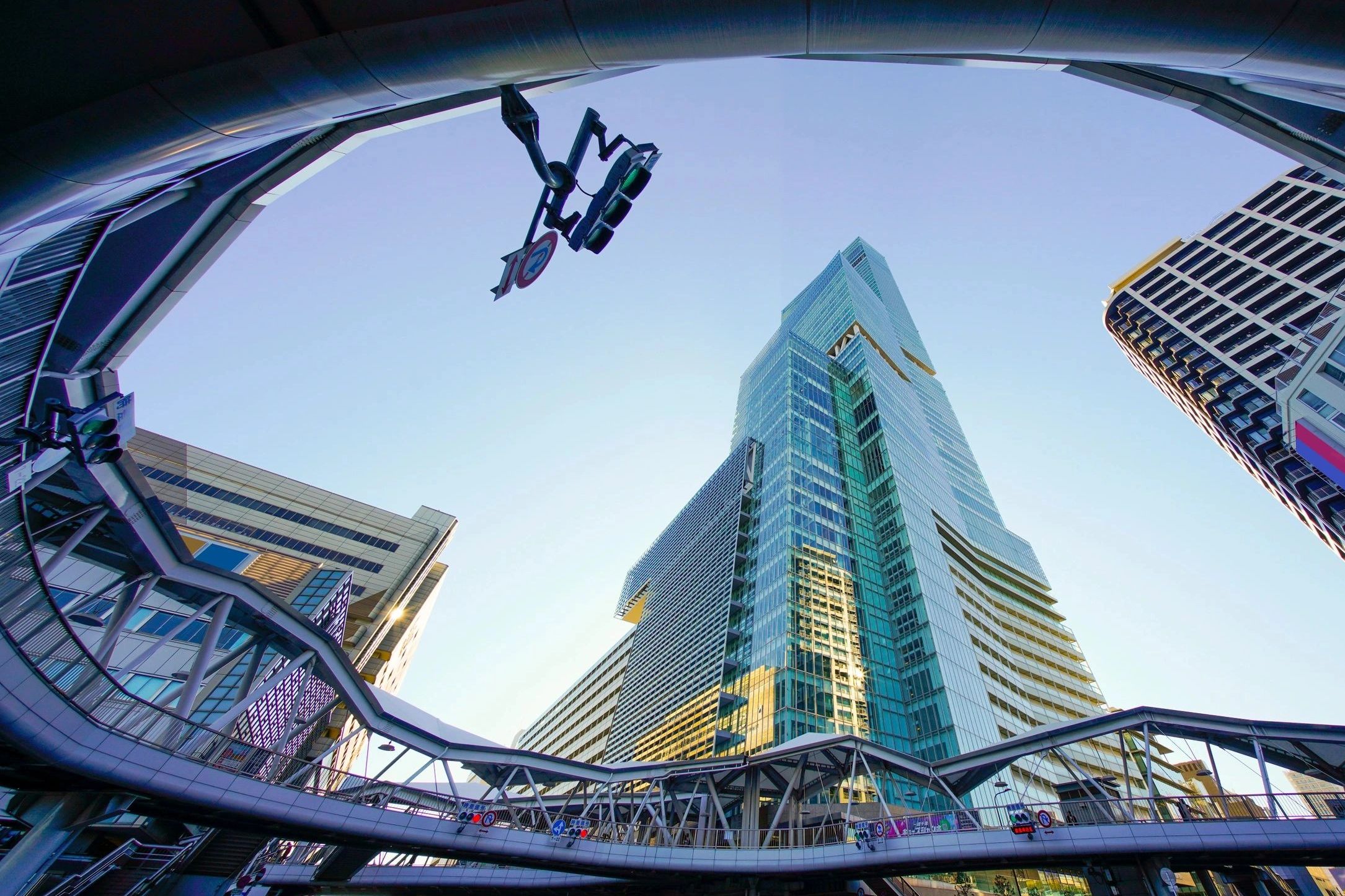 Modern skyscraper viewed through a curved pedestrian bridge and traffic lights.
