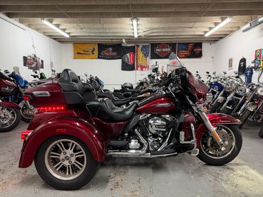 Maroon three-wheeled motorcycle parked inside a showroom with other bikes.