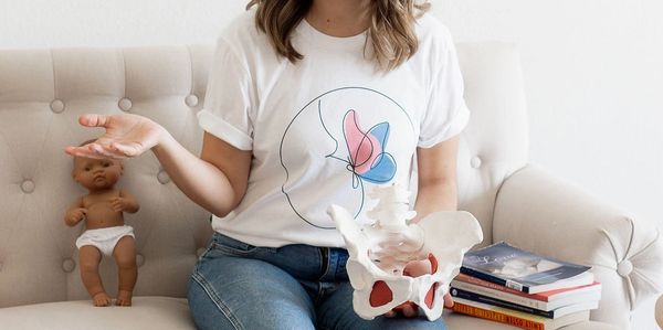 A woman holding a pelvic bone model explains to an audience with a baby doll beside her.