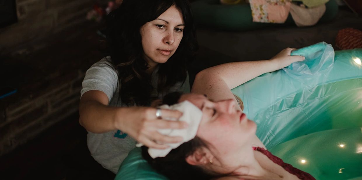 A woman is cared for during water birth in an inflatable birthing pool.