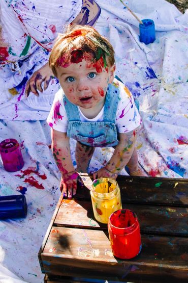Toddler covered in paint during a colorful art activity.