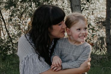 Woman hugging a smiling child outdoors.