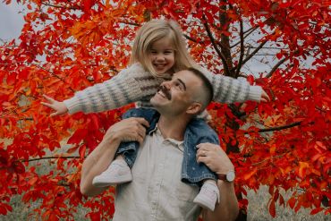Father carrying daughter on shoulders in autumn.
