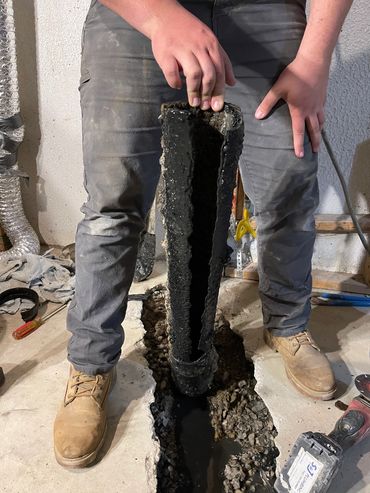 Person holding a split section of dark pipe over a floor opening.