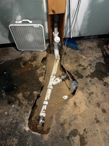 White pipe assembly exposed in a concrete floor trench.