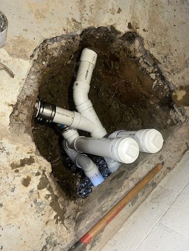 White pipe fittings exposed in an opening in a concrete floor.