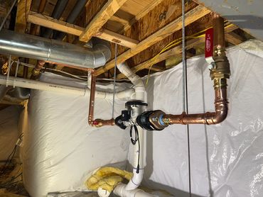 Copper piping, valves and a water meter below basement ceiling joists.