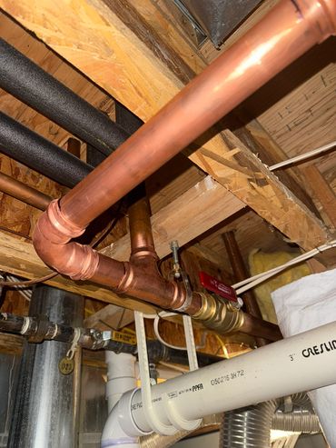 Copper pipe and fittings below exposed floor joists.
