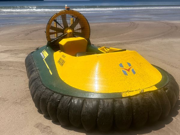A yellow and green hovercraft parked on a sandy beach near the ocean.
