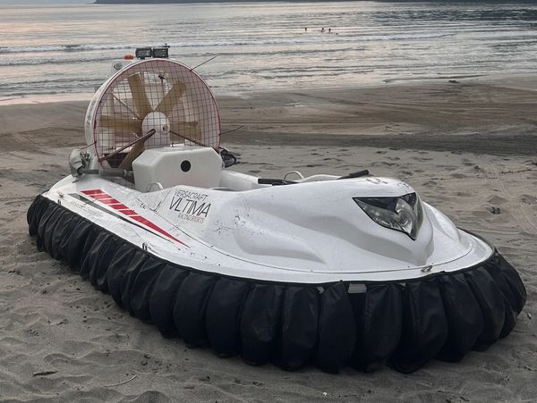 White hovercraft with black skirt parked on sandy beach near water.