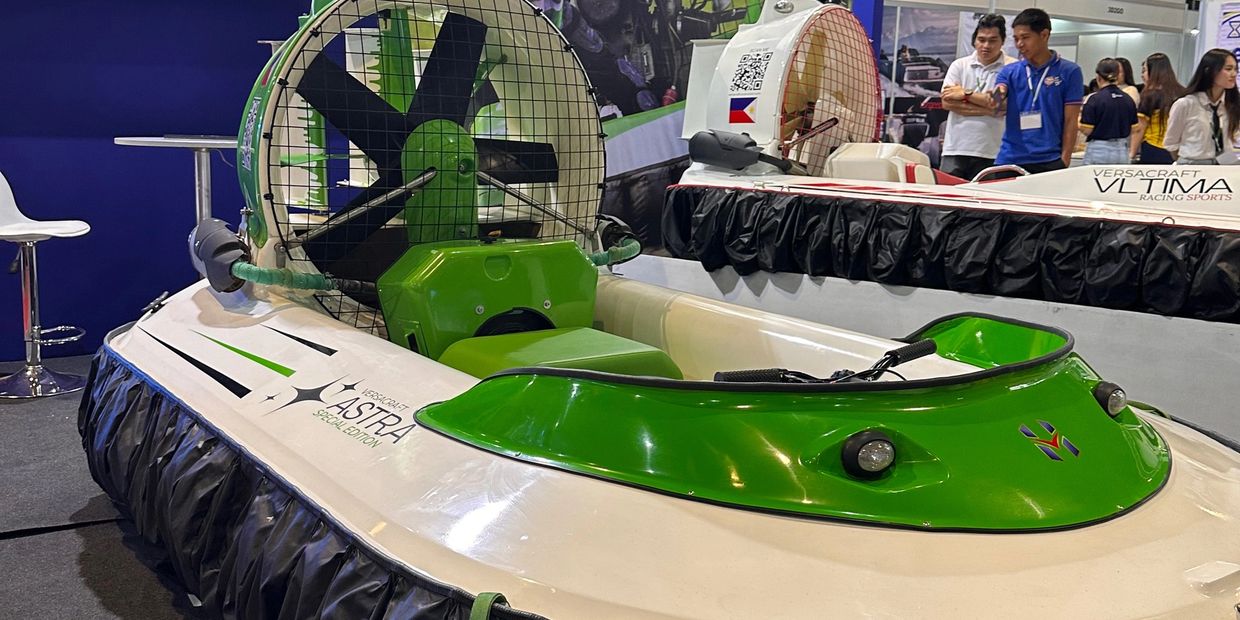 A green and white hovercraft displayed indoors with people in the background.