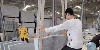 Workers handling large stone slabs in an industrial warehouse.