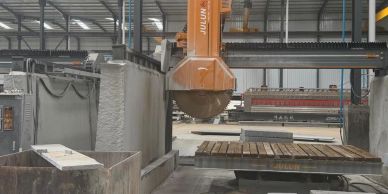 Industrial stone cutting machine slicing large stone slabs in a factory.