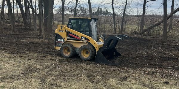 Yellow skid steer loader parked near trees on a cloudy day.